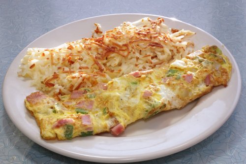 A plate with a ham and vegetable omelet alongside crispy golden hash browns.