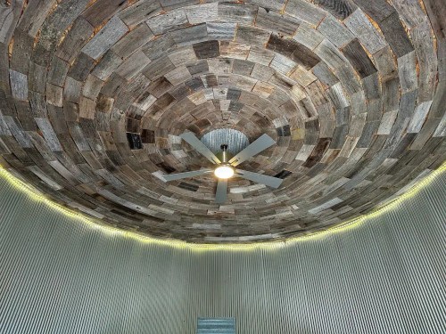 Interior view of a circular room with a wooden, spiraled ceiling and a ceiling fan, illuminated by soft lights.