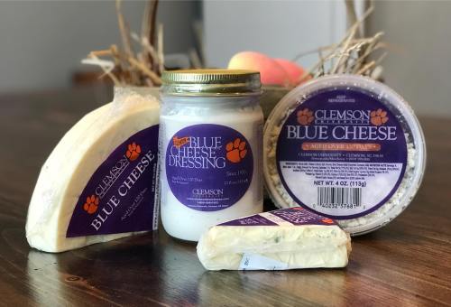 A collection of Clemson University blue cheese products, including cheese, dressing, and packaging, on a wooden surface.
