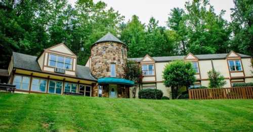 A stone and wood building with a tower, surrounded by green trees and a grassy lawn.