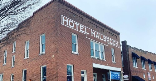 Brick building with "Hotel Halbrook" painted on the side, featuring large windows and a cloudy sky above.
