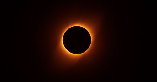 A solar eclipse with a glowing corona surrounding the dark silhouette of the moon against a black sky.