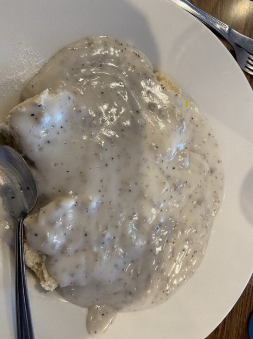 A plate of biscuits covered in creamy sausage gravy, with a spoon resting beside it.
