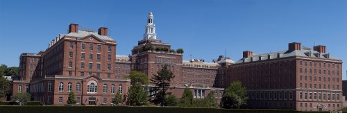Historic brick building with a clock tower, surrounded by greenery and a clear blue sky.