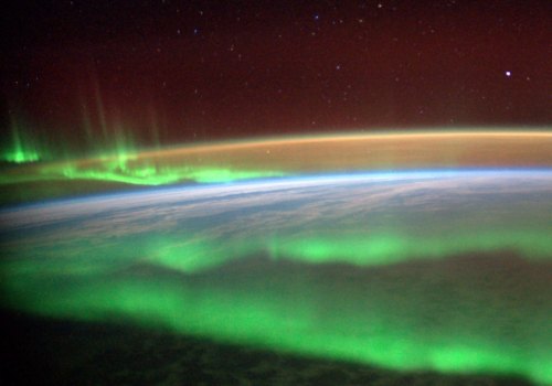 A stunning view of Earth from space, showcasing vibrant green auroras against a dark sky filled with stars.