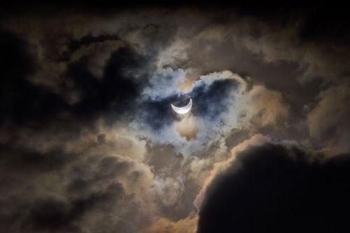 A crescent moon partially obscured by dark, swirling clouds against a dramatic sky.