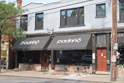 Exterior of a restaurant named "padrino," featuring black awnings and outdoor seating on a sunny day.