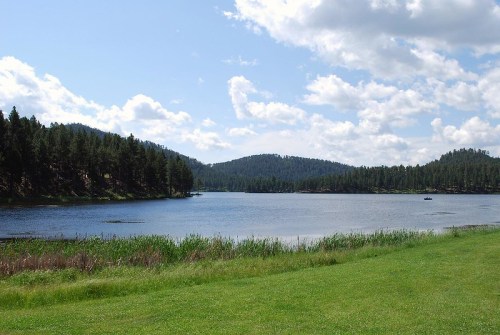 A serene lake surrounded by lush green hills and trees under a partly cloudy sky.