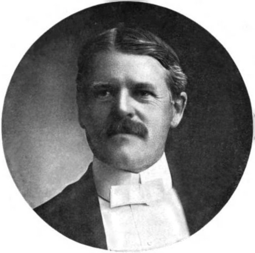 Black and white portrait of a man with a mustache, wearing a bow tie and formal attire, set in a circular frame.