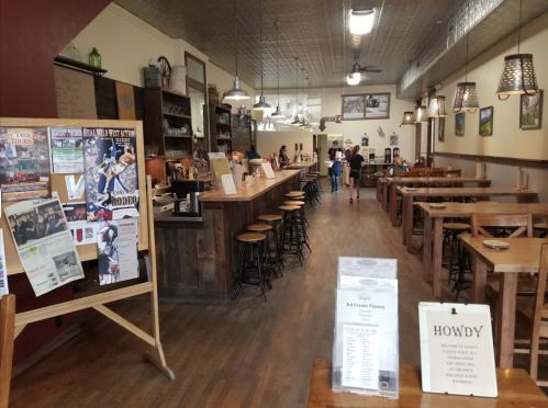 Interior of a rustic ice cream shop with wooden tables, a long bar, and newspaper clippings on the wall.