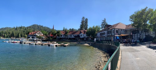 Scenic lakeside view with boats, charming buildings, and trees under a clear blue sky.