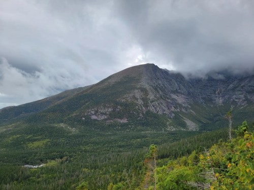 A scenic view of a mountain surrounded by dense forest under a cloudy sky.