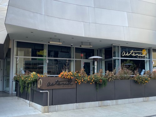 Exterior of a modern restaurant named "asterid," featuring a patio with plants and outdoor heaters.