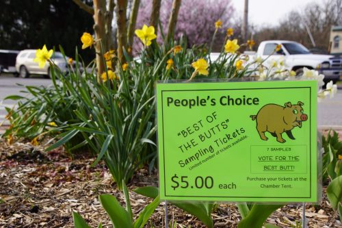 A bright green sign advertising "Best of the Butts" sampling tickets for $5, surrounded by blooming daffodils.