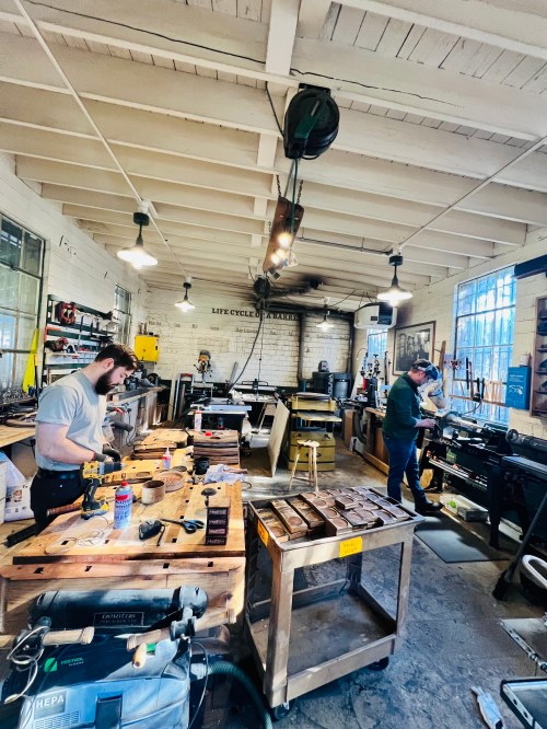 A workshop with two people working on projects, surrounded by tools and equipment in a well-lit space.