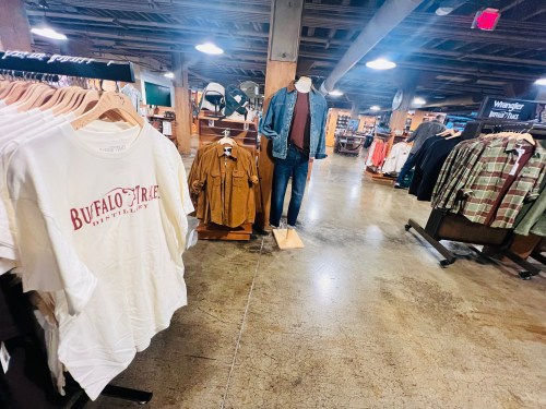 A retail store interior showcasing clothing displays, including shirts, jackets, and jeans on mannequins and racks.