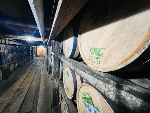 A dimly lit warehouse with wooden barrels stacked on shelves, showcasing aging whiskey.