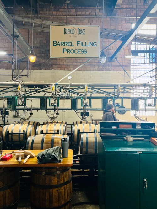 Inside Buffalo Trace Distillery, a worker oversees the barrel filling process with stacked barrels and equipment.