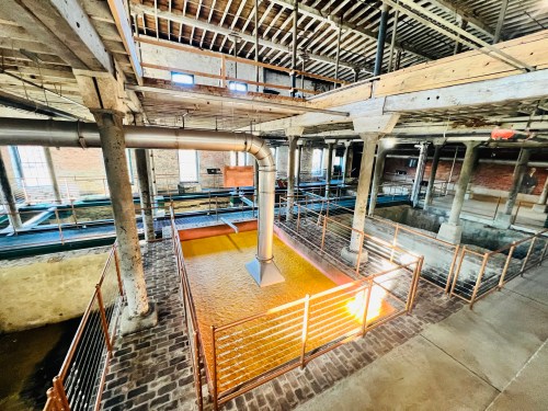 Interior of an industrial building featuring a large, orange-tinted pool of liquid surrounded by metal railings and beams.