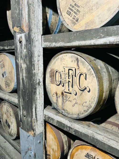 Wooden barrels stacked in a warehouse, featuring the initials "O.F.C." on the front of one barrel.