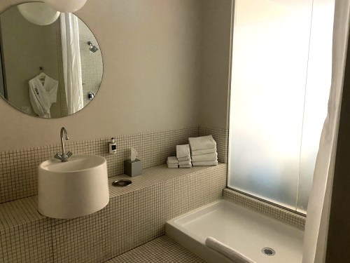 Modern bathroom featuring a round mirror, a minimalist sink, and neatly stacked towels beside a glass shower.