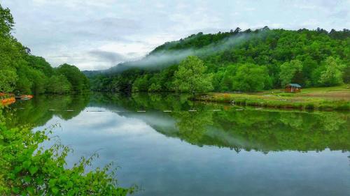 A serene lake surrounded by lush green trees and misty hills, reflecting the landscape in calm waters.
