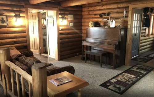 Cozy log cabin interior featuring a piano, sofa, and rustic decor with warm lighting.