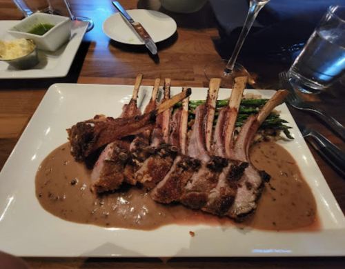 A plate of roasted lamb chops with a rich sauce, served alongside asparagus and a side of mashed potatoes.
