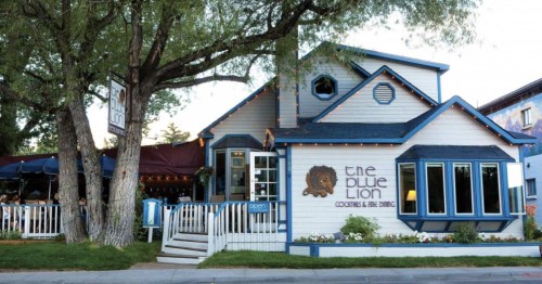 A charming restaurant with a lion logo, featuring a white exterior, blue accents, and outdoor seating under trees.
