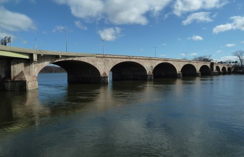 A stone bridge with multiple arches spans a river under a blue sky with scattered clouds.