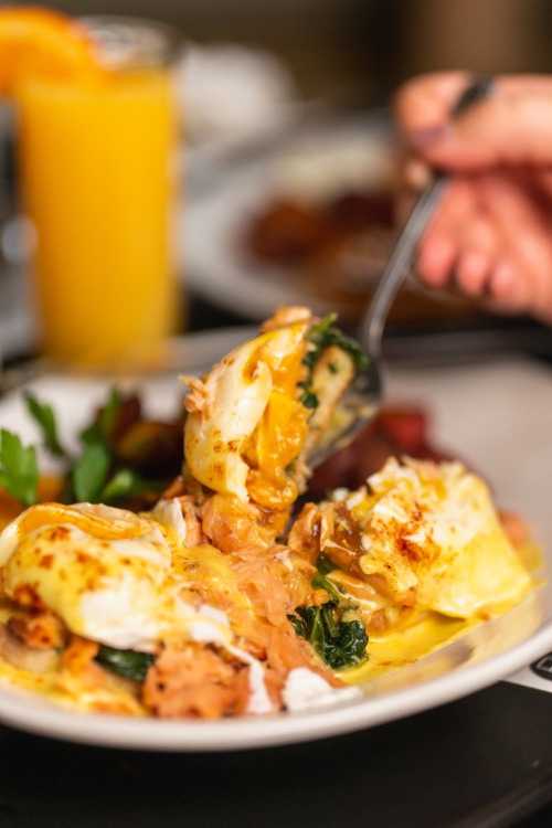 A close-up of a plate with eggs Benedict, topped with salmon and cheese, alongside a glass of orange juice.