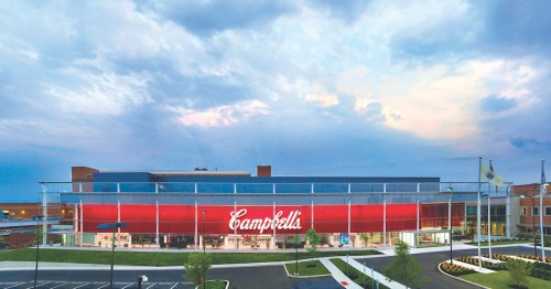 Exterior view of the Campbell's Soup Company building, featuring a large red sign and a cloudy sky.