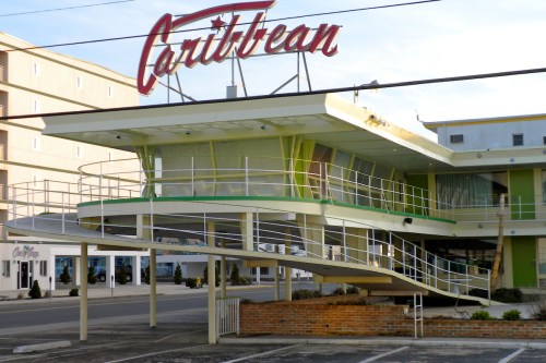 A retro-style motel with a bright yellow and green exterior, featuring a distinctive overhanging sign that reads "Caribbean."