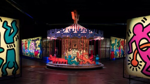 Colorful carousel surrounded by vibrant, abstract art panels in a dimly lit space.