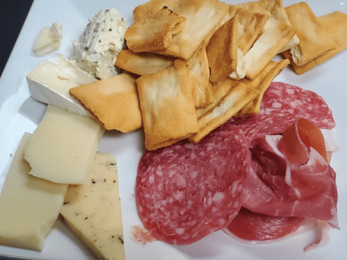 A plate featuring assorted cheeses, cured meats, and crispy crackers.