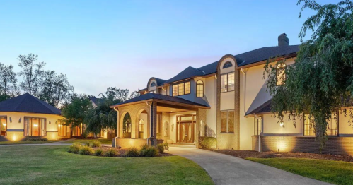 A spacious, modern home with a large entrance, surrounded by landscaped grounds at dusk.