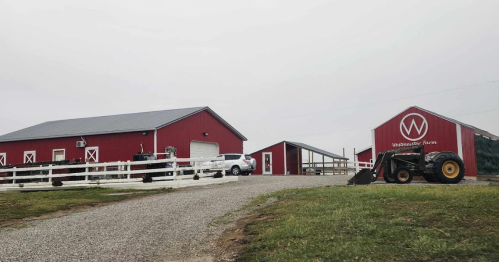 A red barn and farm buildings with a gravel driveway, a tractor, and a cloudy sky in the background.