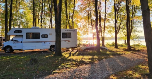 An RV parked among trees at sunset, with a serene lake visible in the background.