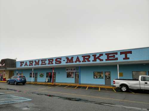 A blue building with a large sign reading "FARMERS-MARKET" and parked cars in front on a cloudy day.