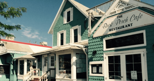 A charming teal building with white trim, featuring a sign for "The Back Porch Cafe Restaurant" and a sunny blue sky.