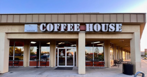 Exterior of a coffee house with large signage, glass doors, and outdoor seating under a clear sky.
