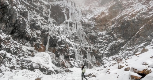 A person stands in a snowy landscape, surrounded by rocky cliffs and frozen waterfalls.