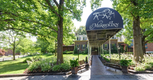 A charming inn entrance with a covered walkway, surrounded by lush greenery and flower beds.