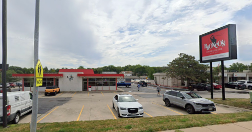 A fast-food restaurant with a red roof and sign, surrounded by parked cars and a cloudy sky.