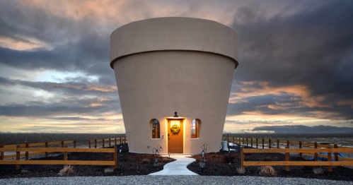 A unique, round building resembling a large cup, set against a dramatic sky at sunset. Pathway leads to the entrance.