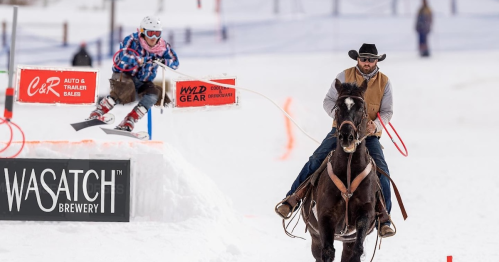 A skier jumps over a barrier while a cowboy rides a horse in a snowy landscape.