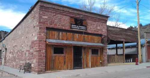 A rustic stone building with wooden accents, featuring a sign for a bar or restaurant, set in a small town.