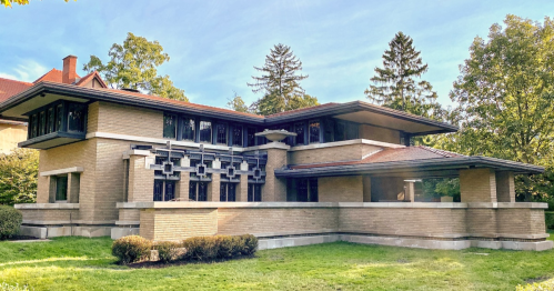 A modernist brick house with large windows and a flat roof, surrounded by greenery and trees.