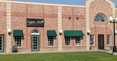 Exterior of Copper Grill restaurant, featuring a brick facade, green awnings, and decorative lamps on a sunny day.