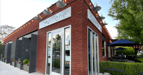 Exterior of a brick restaurant named "cafeniche," featuring outdoor seating and decorative lighting.